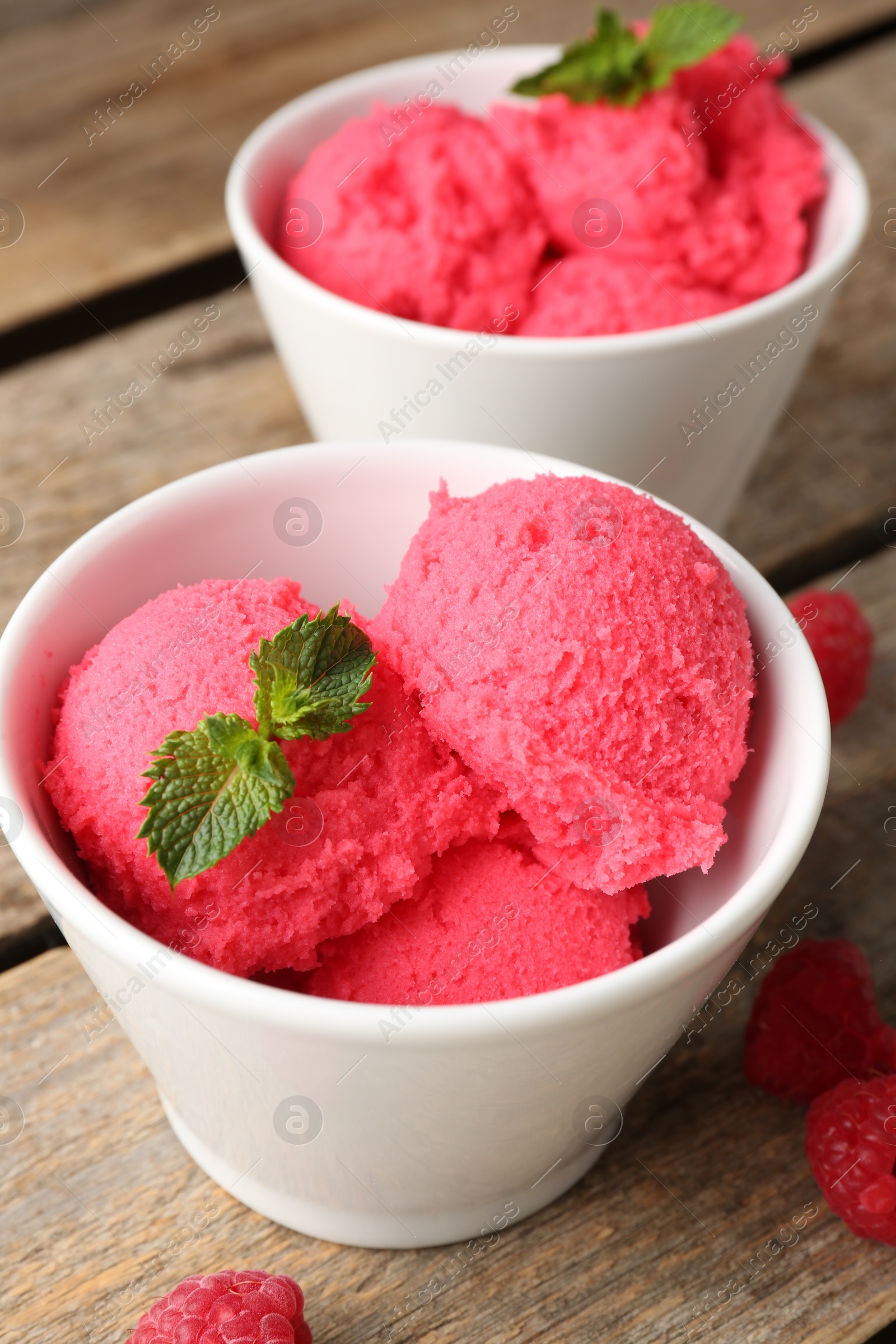 Photo of Delicious raspberry sorbet with mint in bowls and fresh berries on wooden table, closeup