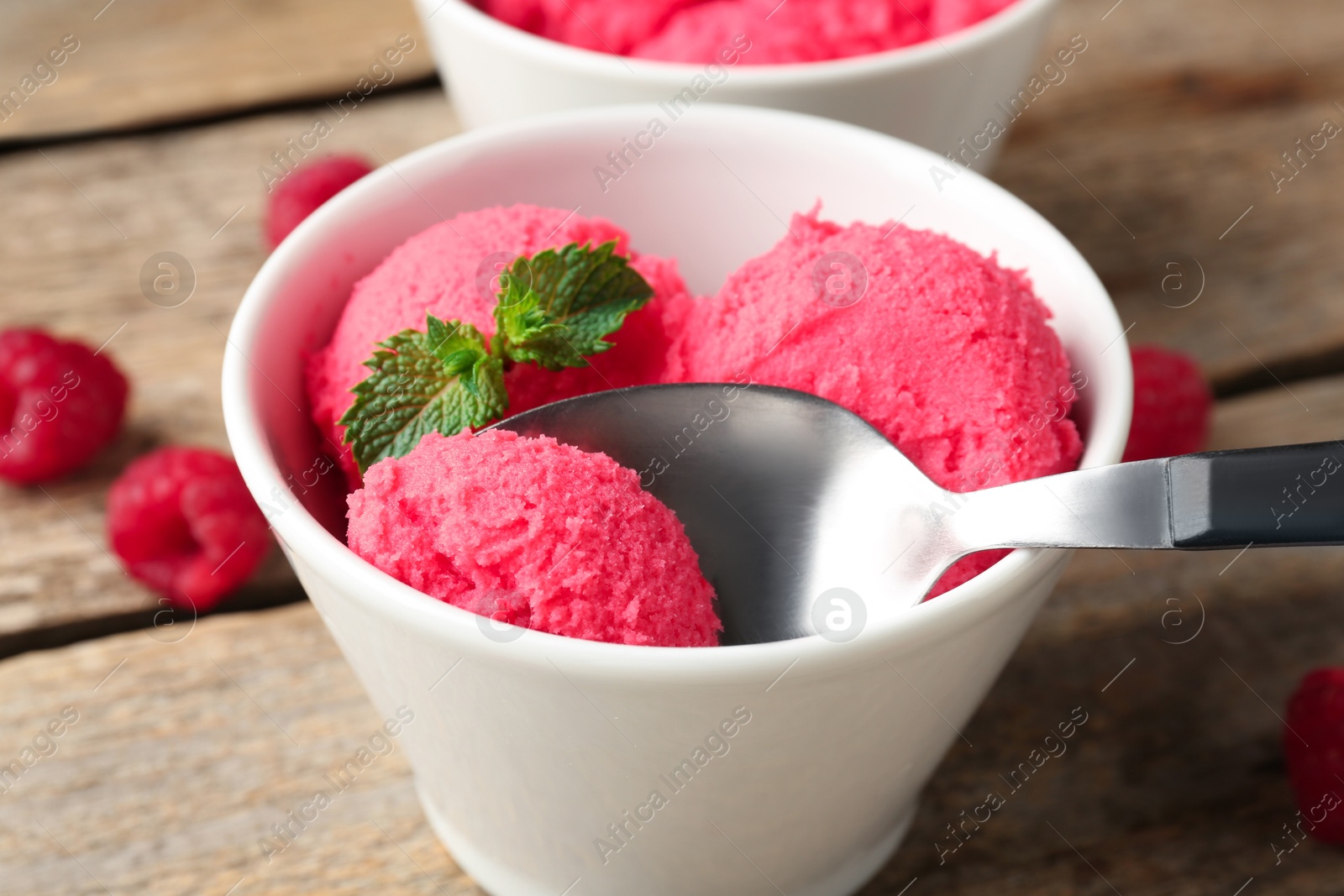 Photo of Taking delicious raspberry sorbet with mint from bowl with spoon at wooden table, closeup