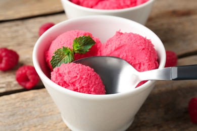Photo of Taking delicious raspberry sorbet with mint from bowl with spoon at wooden table, closeup