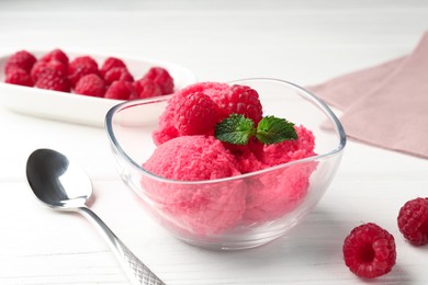Photo of Delicious raspberry sorbet with mint in bowl, spoon and fresh berries on white wooden table, closeup