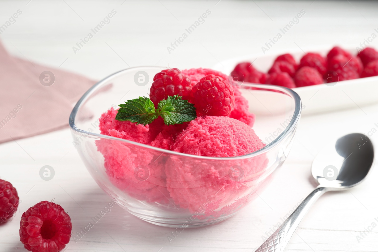 Photo of Delicious raspberry sorbet with mint in bowl, spoon and fresh berries on white wooden table, closeup