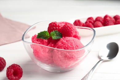 Photo of Delicious raspberry sorbet with mint in bowl, spoon and fresh berries on white wooden table, closeup
