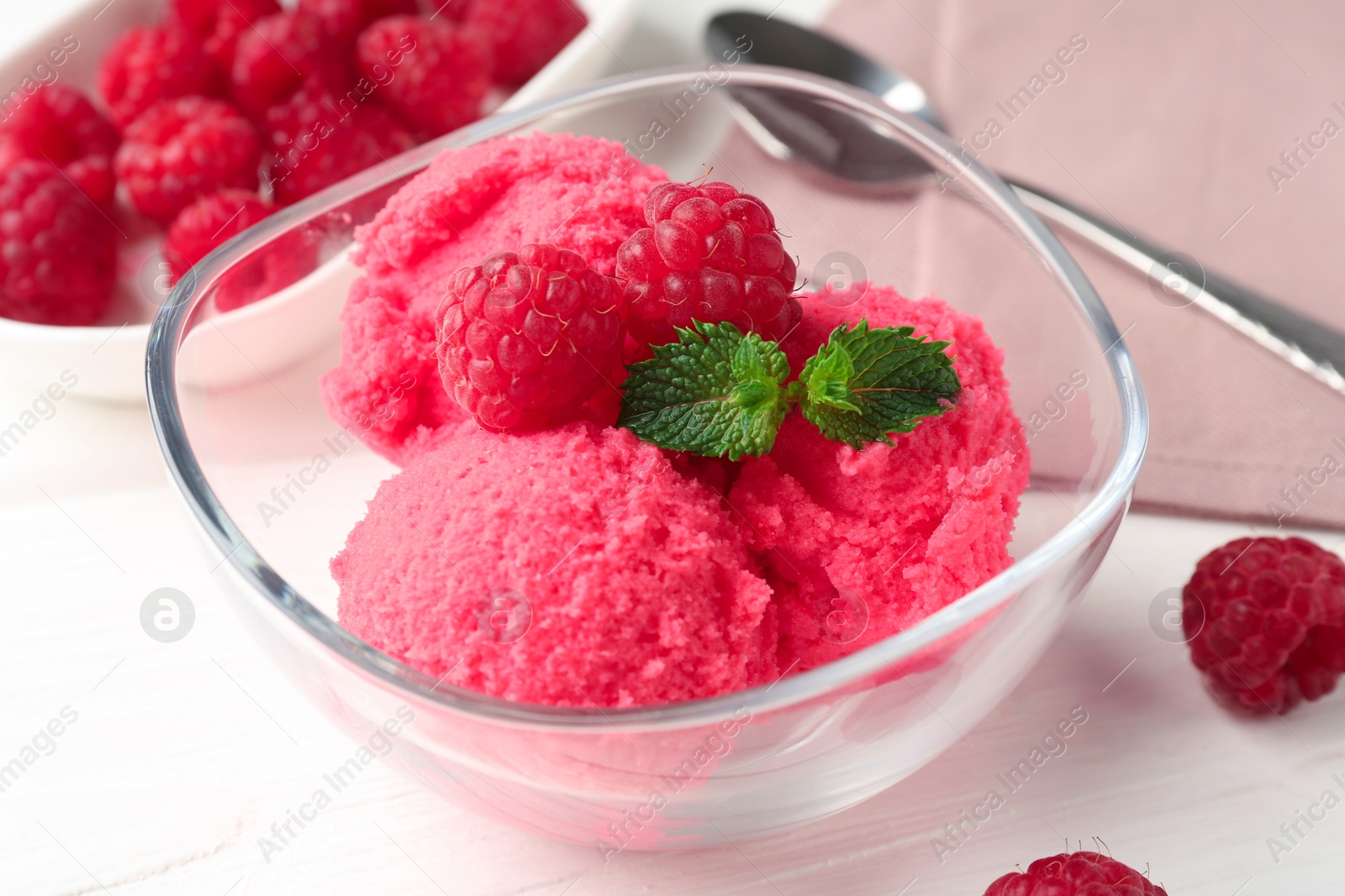 Photo of Delicious raspberry sorbet with mint in bowl and fresh berries on white wooden table, closeup