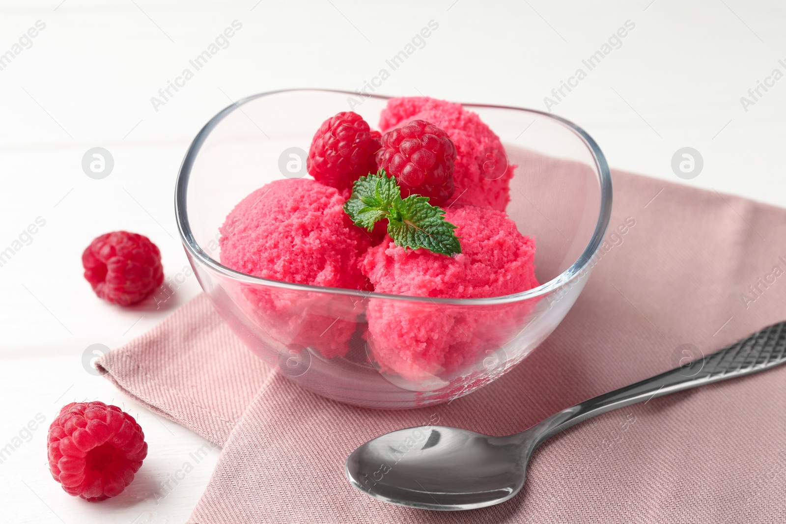 Photo of Delicious raspberry sorbet with mint in bowl, spoon and fresh berries on white wooden table, closeup