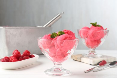 Photo of Delicious raspberry sorbet with mint in dessert bowls and fresh berries on white wooden table against light grey background, closeup