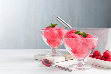 Photo of Delicious raspberry sorbet with mint in dessert bowls, spoons and fresh berries on white wooden table against light grey background, closeup. Space for text