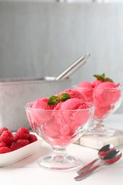 Photo of Delicious raspberry sorbet with mint in dessert bowls, spoons and fresh berries on white wooden table against light grey background, closeup