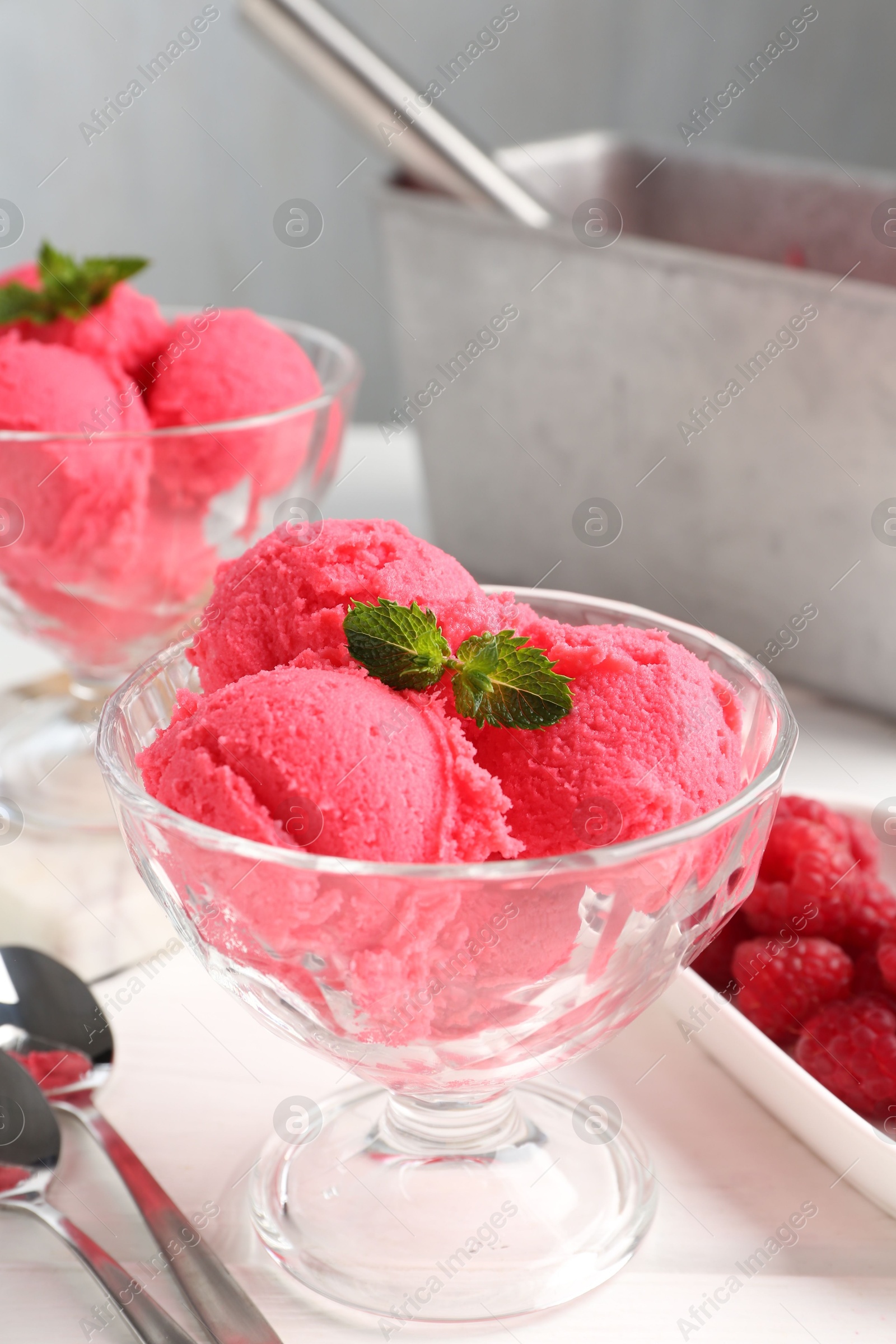 Photo of Delicious raspberry sorbet with mint in dessert bowls, spoons and fresh berries on white wooden table against light grey background, closeup