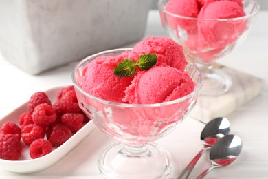 Photo of Delicious raspberry sorbet with mint in dessert bowl, spoons and fresh berries on white wooden table, closeup