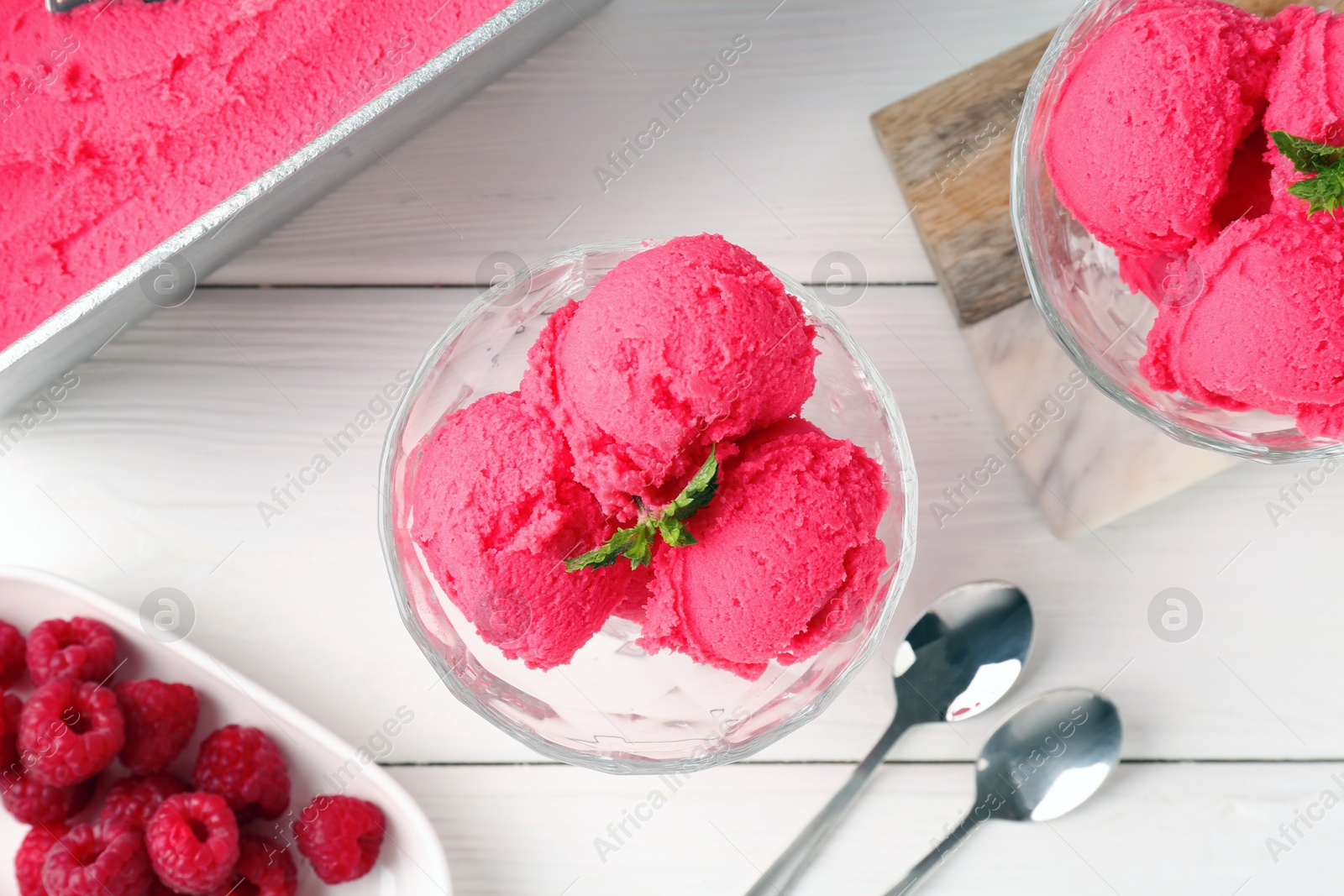 Photo of Delicious raspberry sorbet with mint in dessert bowls, spoons and fresh berries on white wooden table, flat lay