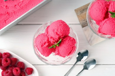 Photo of Delicious raspberry sorbet with mint in dessert bowls, spoons and fresh berries on white wooden table, flat lay