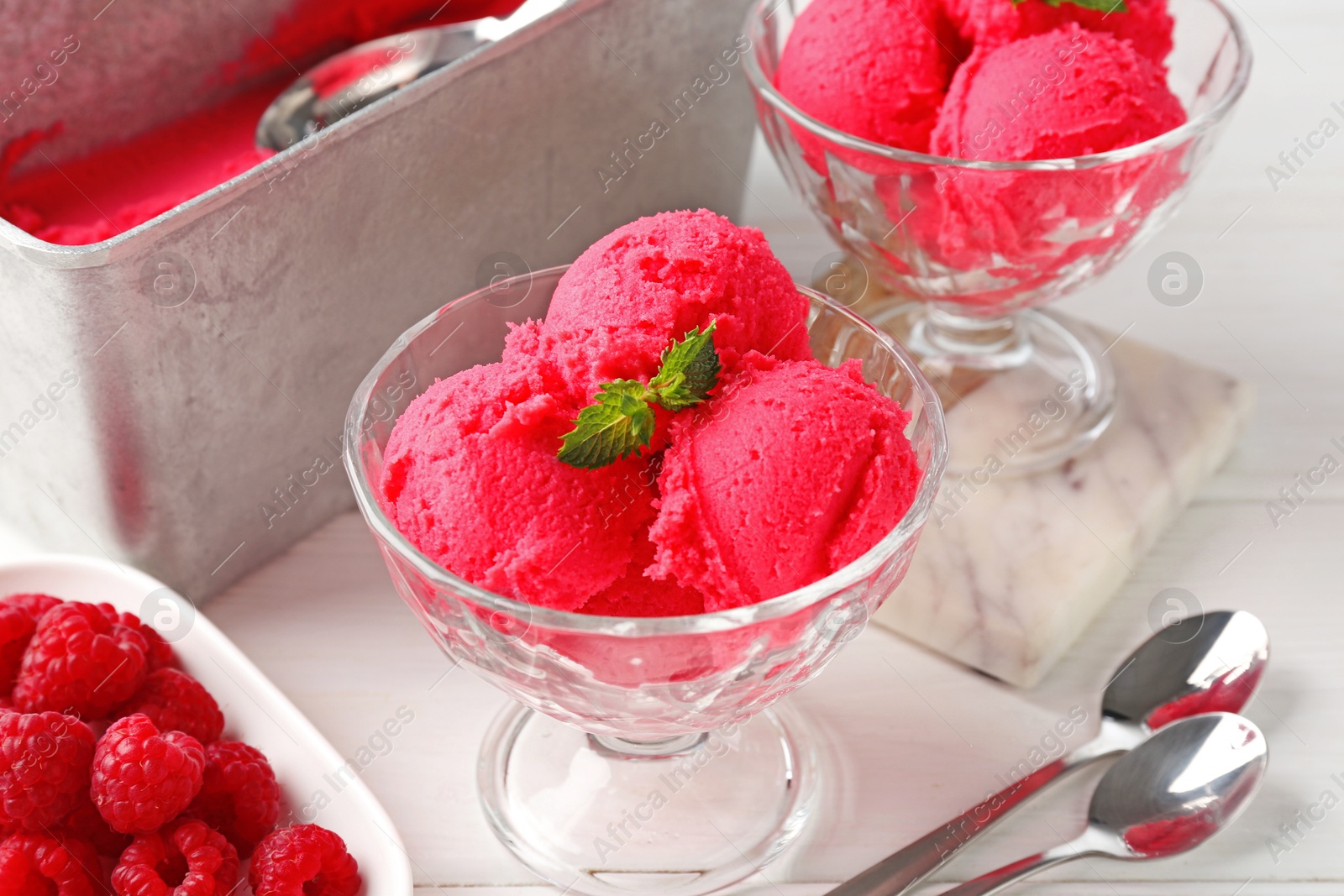 Photo of Delicious raspberry sorbet with mint in dessert bowls, spoons and fresh berries on white wooden table, closeup