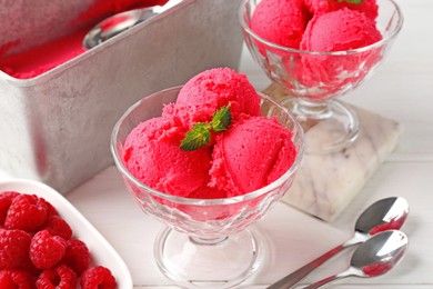 Photo of Delicious raspberry sorbet with mint in dessert bowls, spoons and fresh berries on white wooden table, closeup