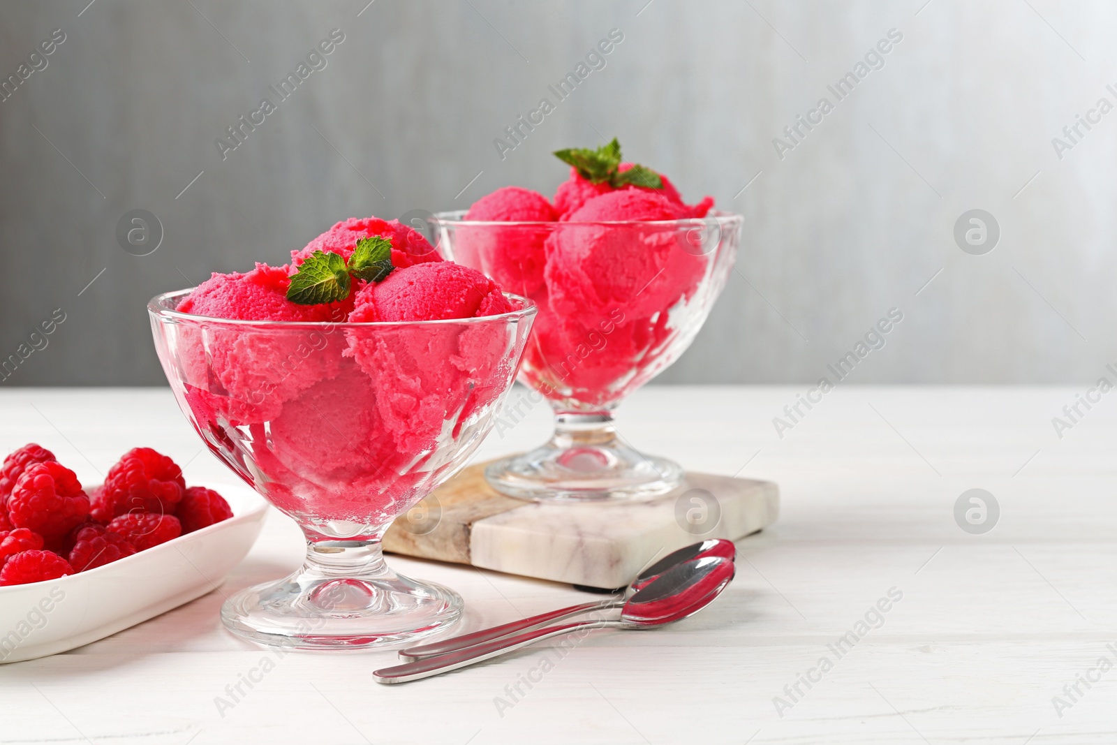 Photo of Delicious raspberry sorbet with mint in dessert bowls, spoons and fresh berries on white wooden table against light grey background, closeup