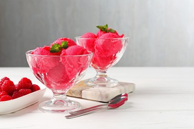 Photo of Delicious raspberry sorbet with mint in dessert bowls, spoons and fresh berries on white wooden table against light grey background, closeup