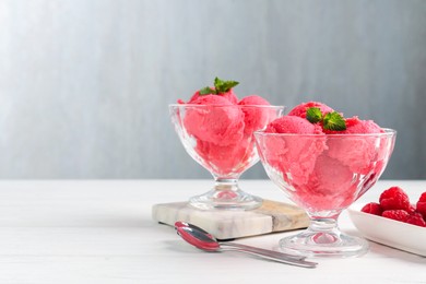 Photo of Delicious raspberry sorbet with mint in dessert bowls, spoons and fresh berries on white wooden table against light grey background, closeup. Space for text