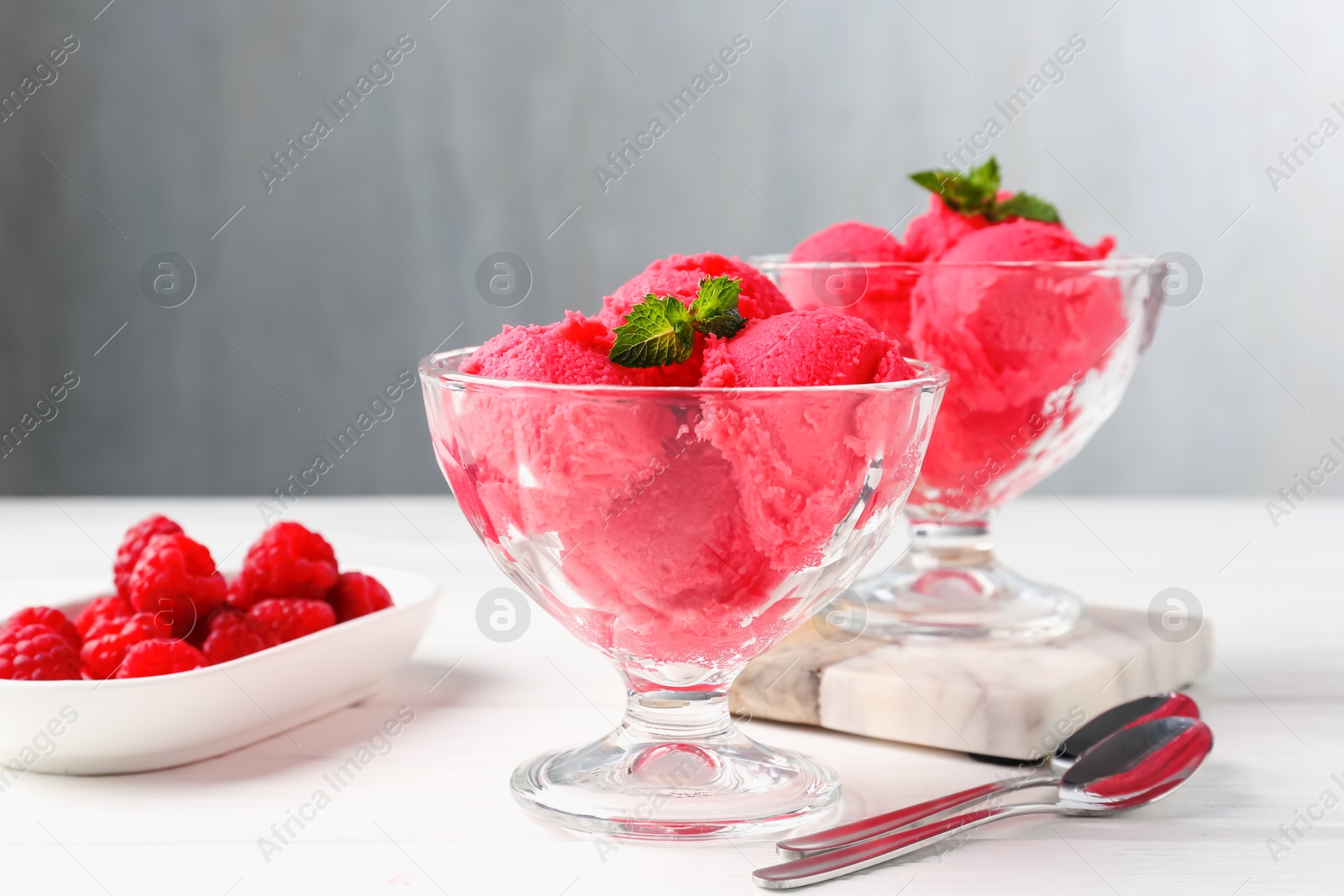 Photo of Delicious raspberry sorbet with mint in dessert bowls, spoons and fresh berries on white wooden table against light grey background, closeup