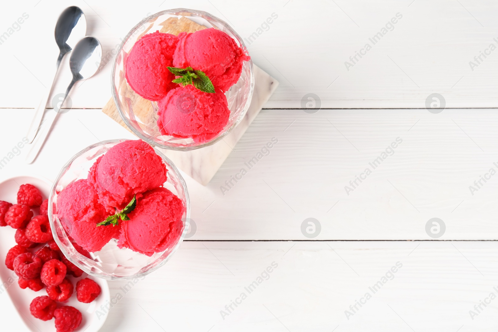 Photo of Delicious raspberry sorbet with mint in dessert bowls, spoons and fresh berries on white wooden table, flat lay. Space for text