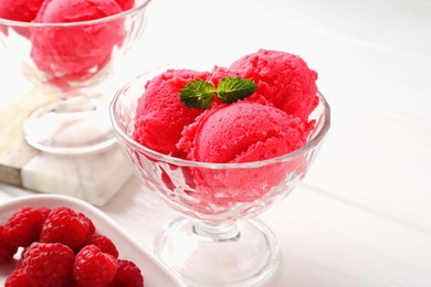Photo of Delicious raspberry sorbet with mint in dessert bowl and fresh berries on white wooden table, closeup