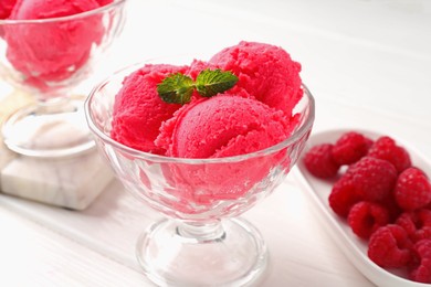 Photo of Delicious raspberry sorbet with mint in dessert bowl and fresh berries on white wooden table, closeup