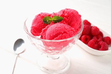 Photo of Delicious raspberry sorbet with mint in dessert bowl, spoon and fresh berries on white wooden table, closeup