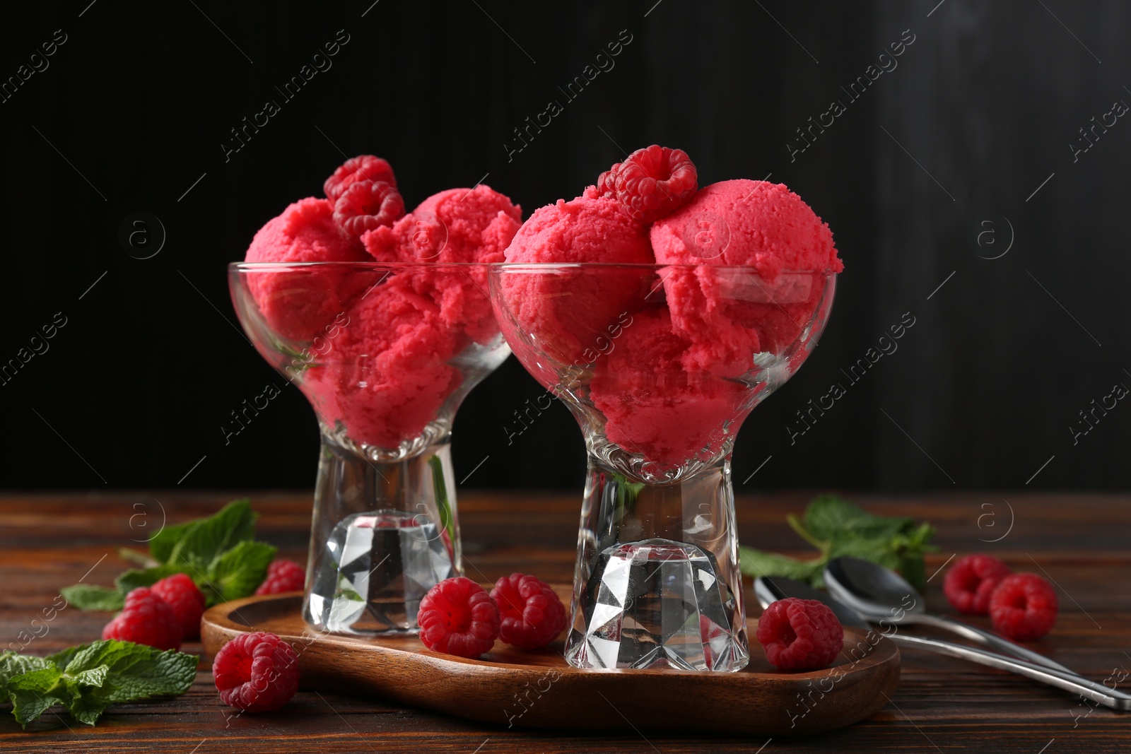 Photo of Delicious raspberry sorbet in dessert bowls, mint and fresh berries on wooden table against black background, closeup