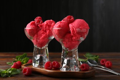 Photo of Delicious raspberry sorbet in dessert bowls, mint and fresh berries on wooden table against black background, closeup