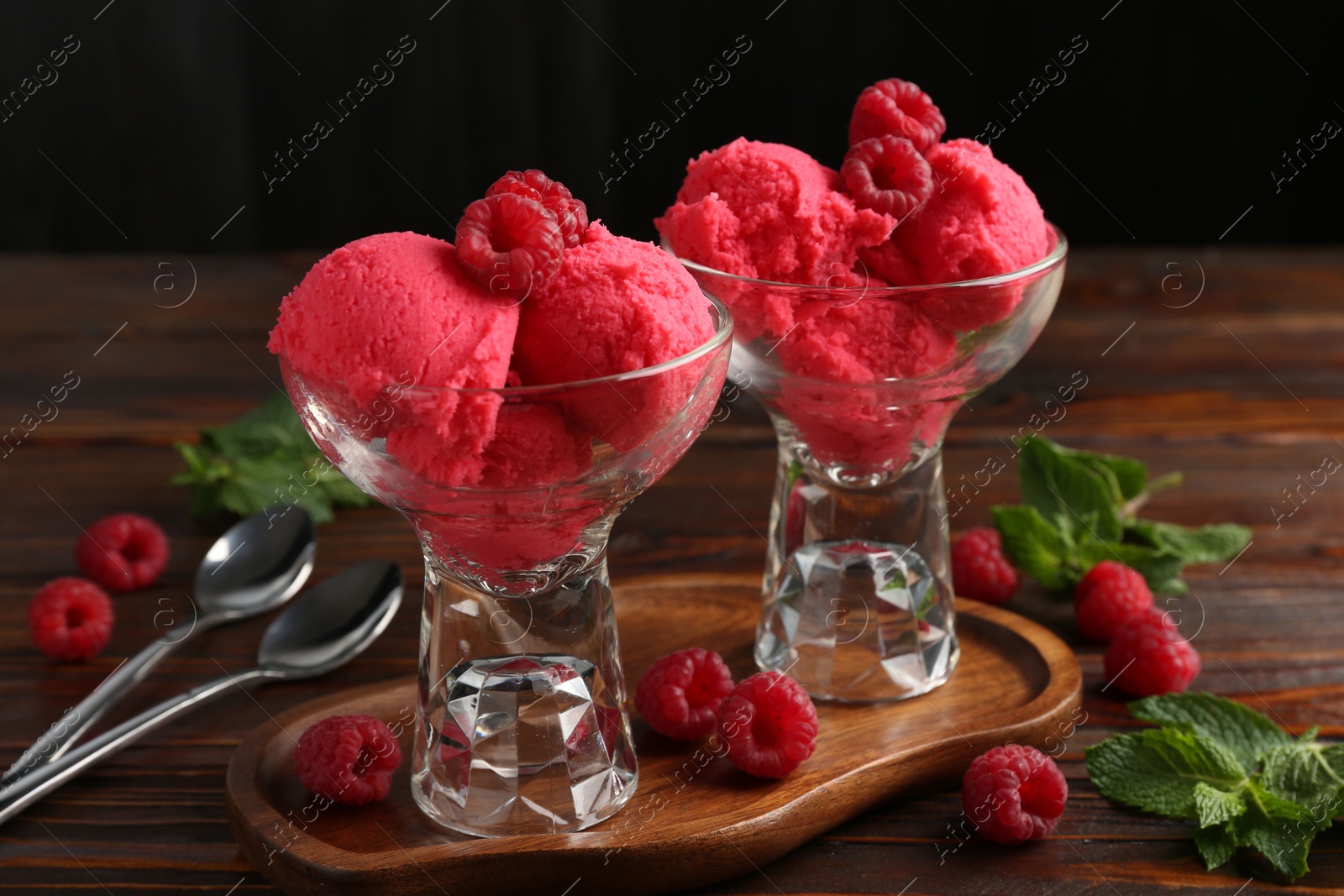 Photo of Delicious raspberry sorbet in dessert bowls, mint and fresh berries on wooden table against black background, closeup