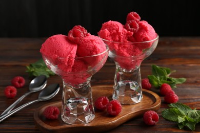 Photo of Delicious raspberry sorbet in dessert bowls, mint and fresh berries on wooden table against black background, closeup