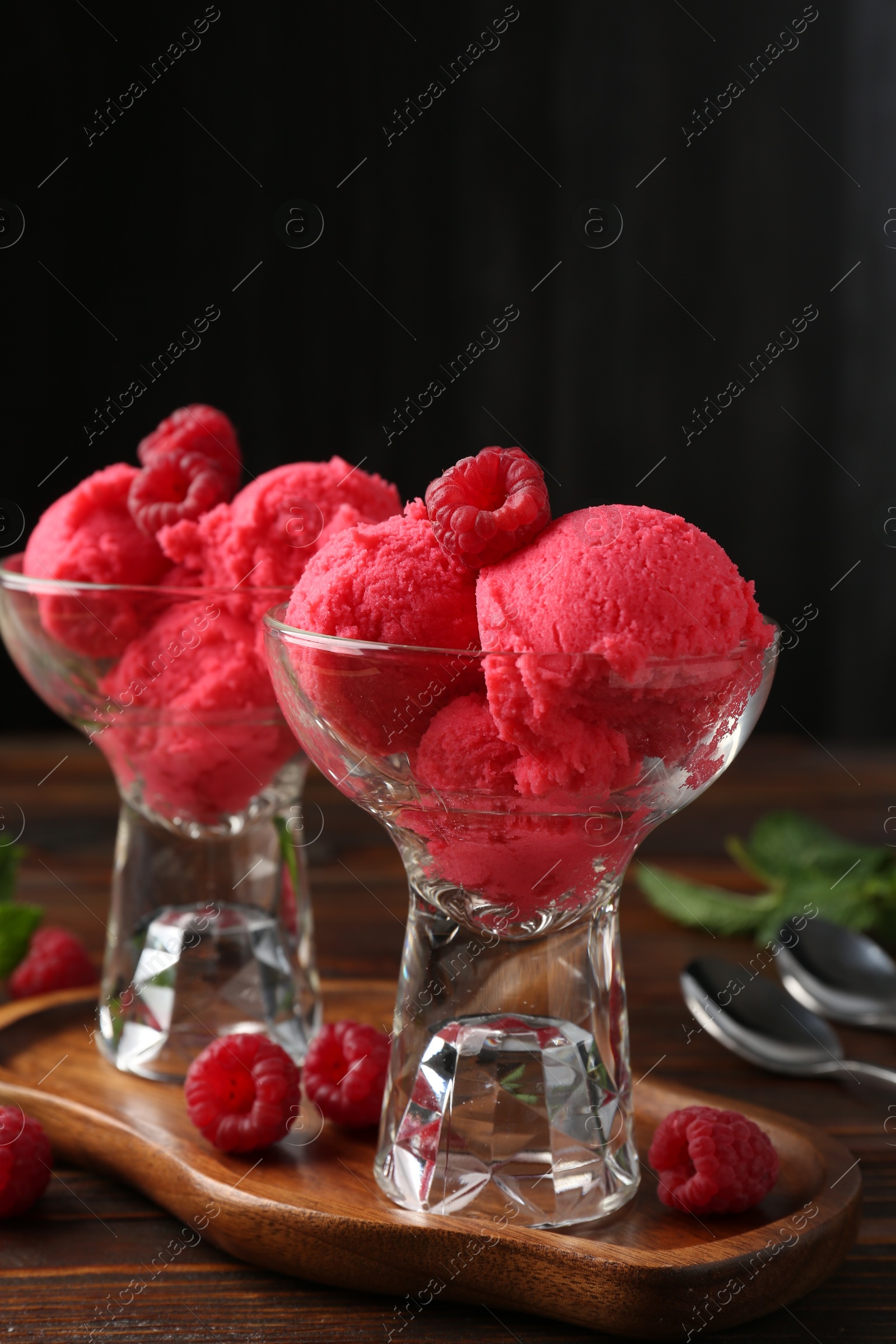 Delicious raspberry sorbet in dessert bowls, mint and fresh berries on wooden table against black background, closeup Photo of Delicious raspberry sorbet in dessert bowls, mint and fresh berries on wooden table against black background, closeup