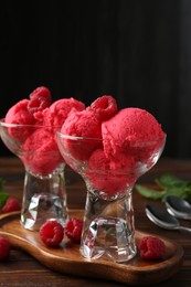 Photo of Delicious raspberry sorbet in dessert bowls, mint and fresh berries on wooden table against black background, closeup
