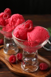 Photo of Delicious raspberry sorbet in dessert bowls and fresh berries on wooden table against black background, closeup