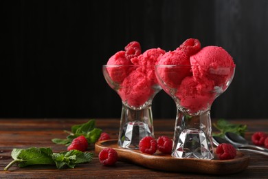 Photo of Delicious raspberry sorbet in dessert bowls, mint and fresh berries on wooden table against black background, closeup