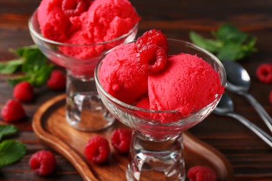 Photo of Delicious raspberry sorbet in dessert bowls, mint and fresh berries on wooden table, closeup