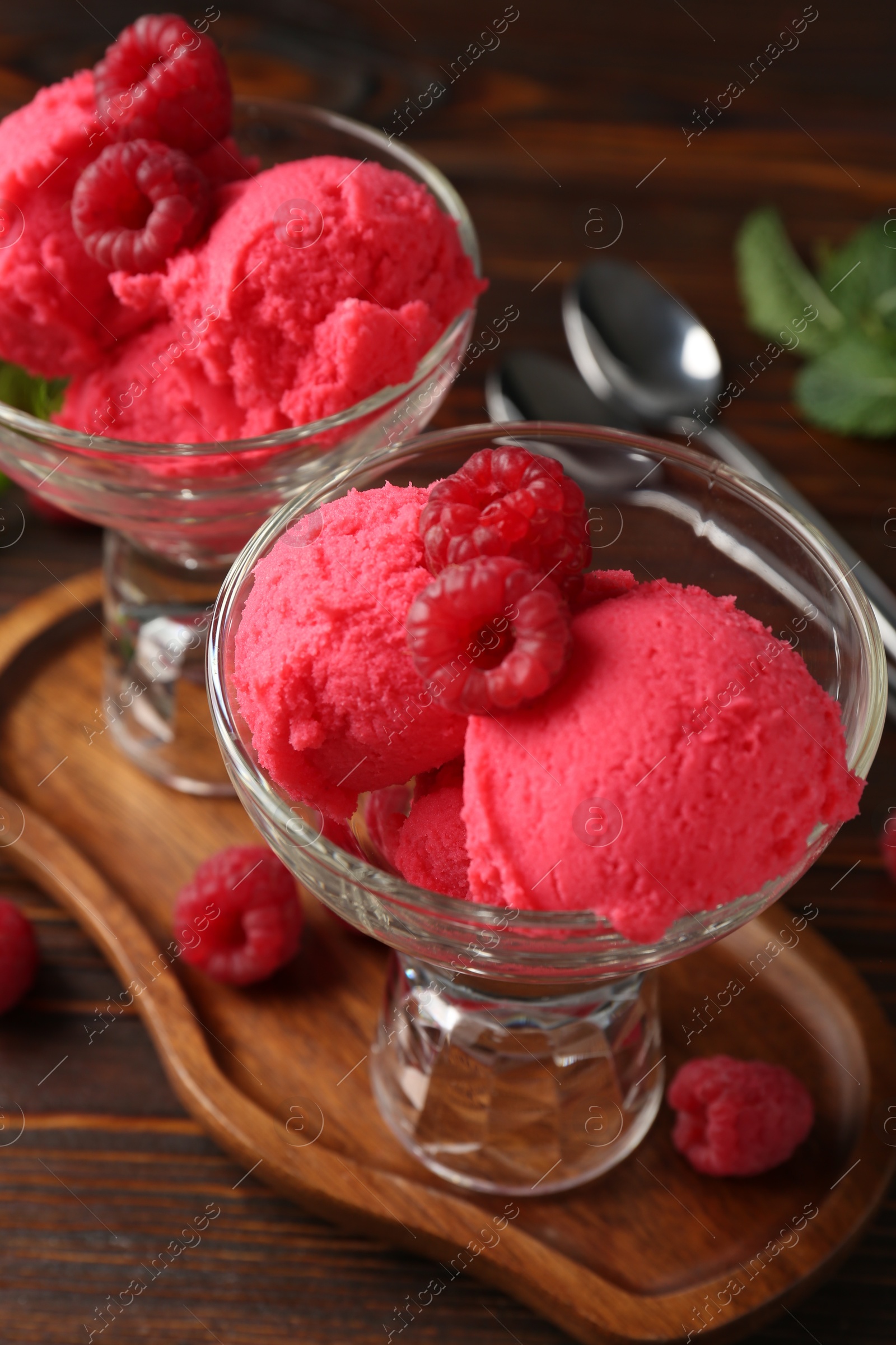 Photo of Delicious raspberry sorbet in dessert bowls, mint and fresh berries on wooden table, closeup
