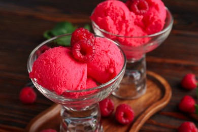 Photo of Delicious raspberry sorbet in dessert bowls and fresh berries on wooden table, closeup