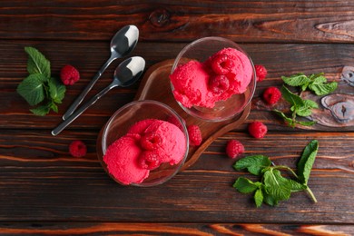 Photo of Delicious raspberry sorbet in dessert bowls, spoons, mint and fresh berries on wooden table, flat lay