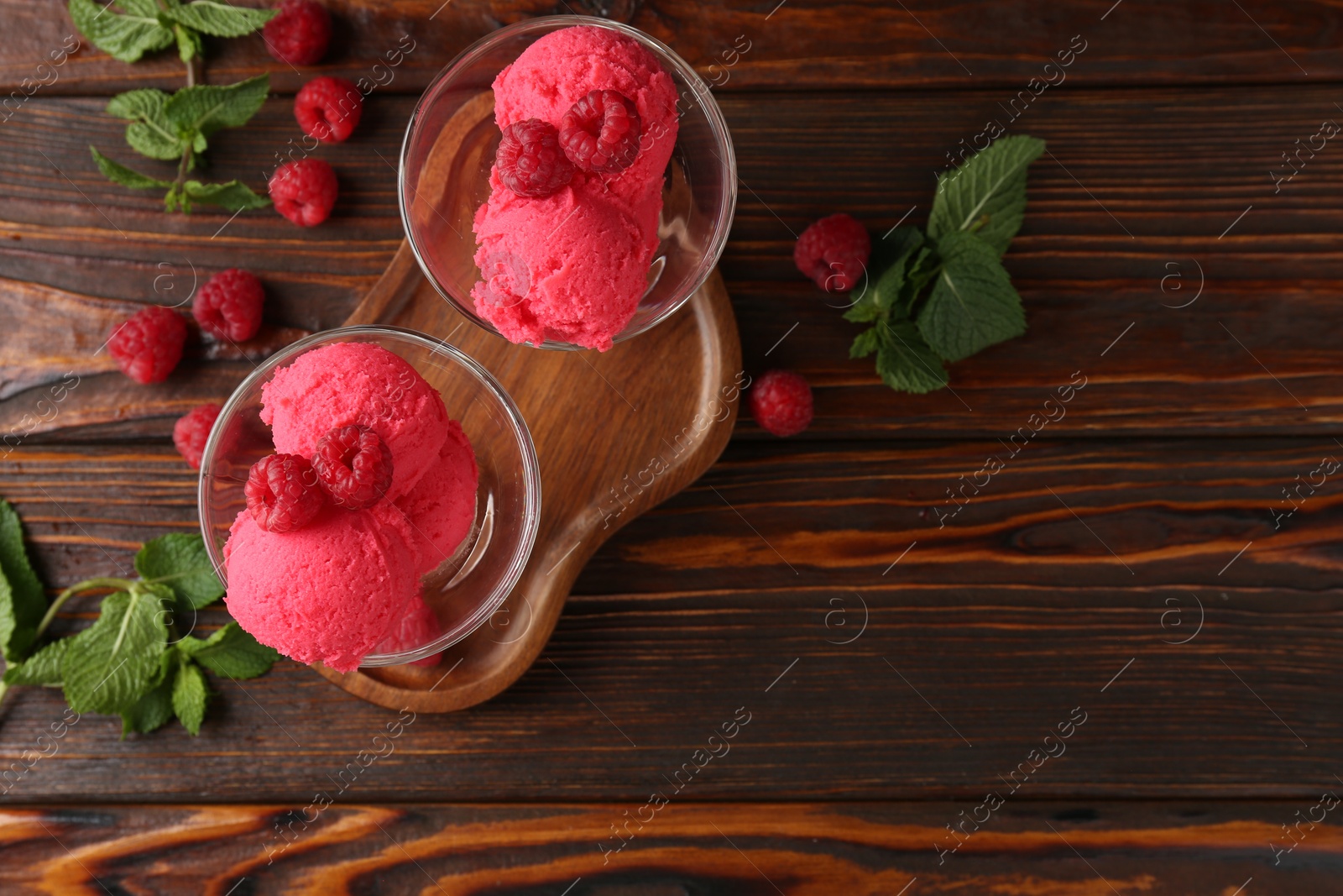Photo of Delicious raspberry sorbet in dessert bowls, mint and fresh berries on wooden table, flat lay. Space for text