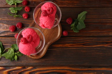 Photo of Delicious raspberry sorbet in dessert bowls, mint and fresh berries on wooden table, flat lay. Space for text