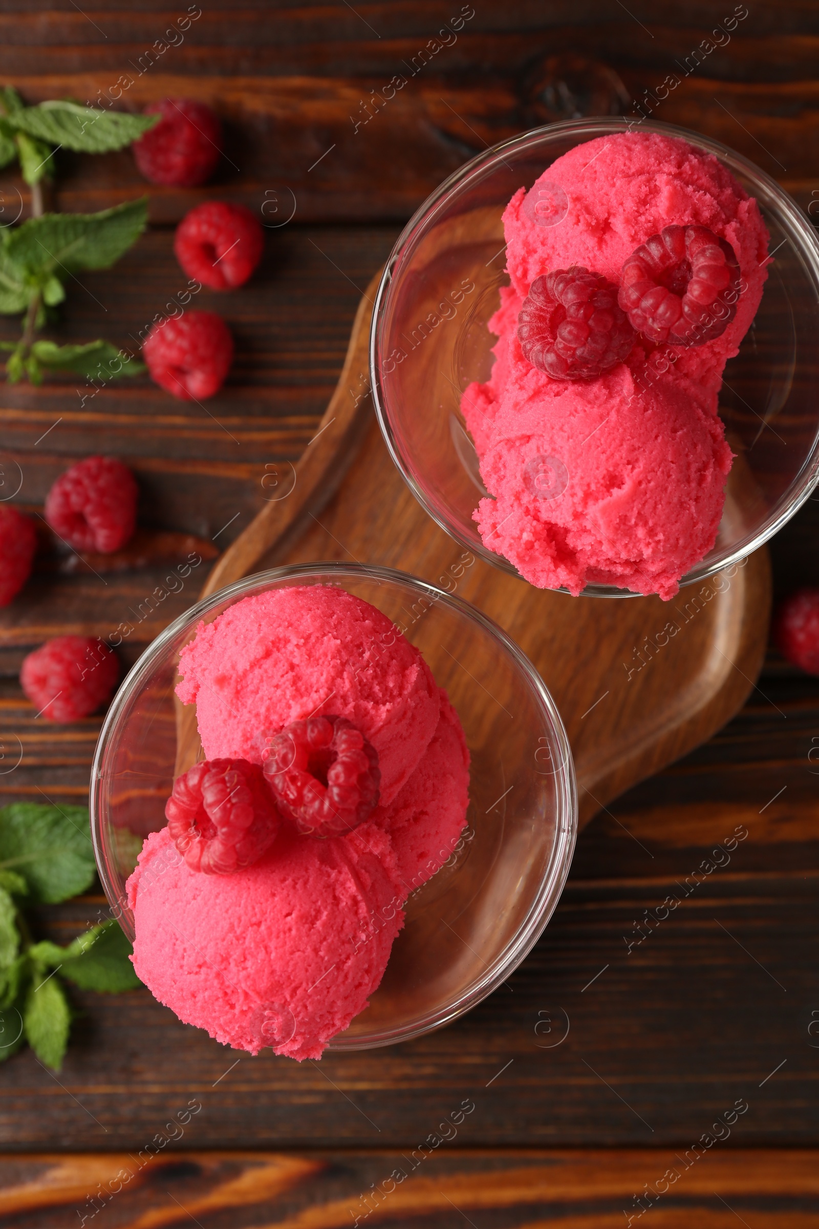 Photo of Delicious raspberry sorbet in dessert bowls, mint and fresh berries on wooden table, flat lay