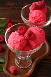 Photo of Delicious raspberry sorbet and fresh berries in dessert bowls on wooden table, closeup