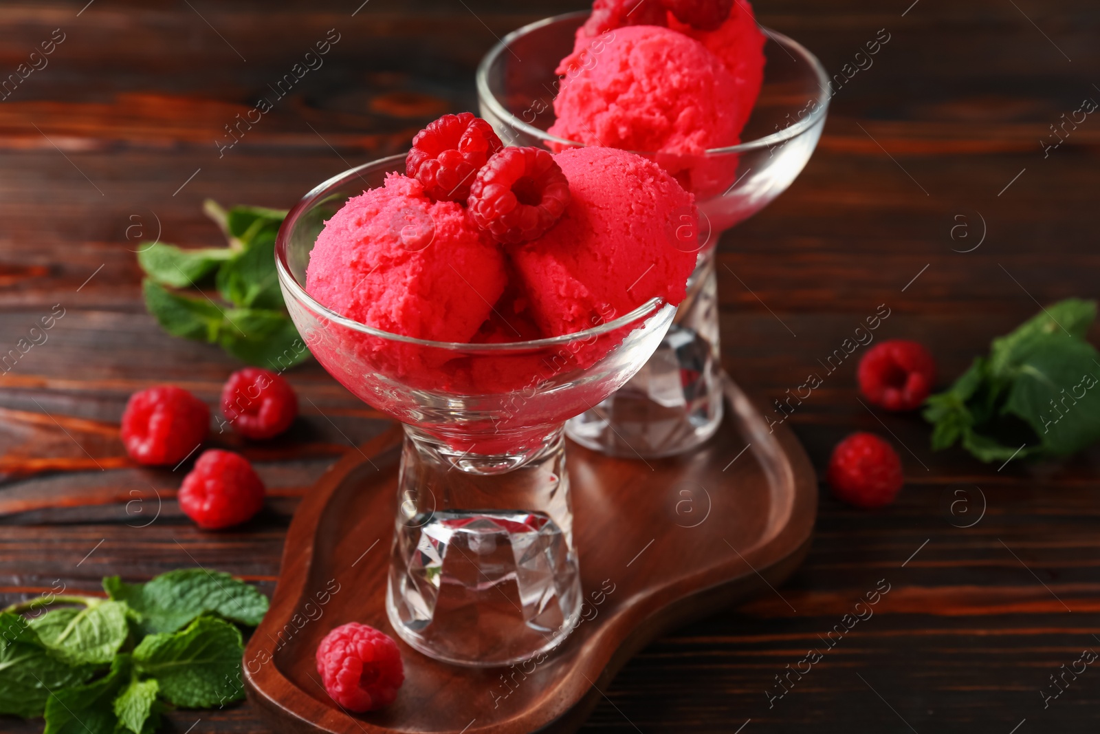 Photo of Delicious raspberry sorbet in dessert bowls, mint and fresh berries on wooden table, closeup