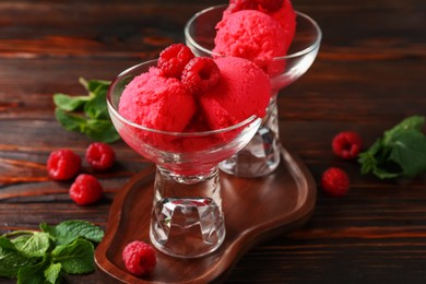 Photo of Delicious raspberry sorbet in dessert bowls, mint and fresh berries on wooden table, closeup
