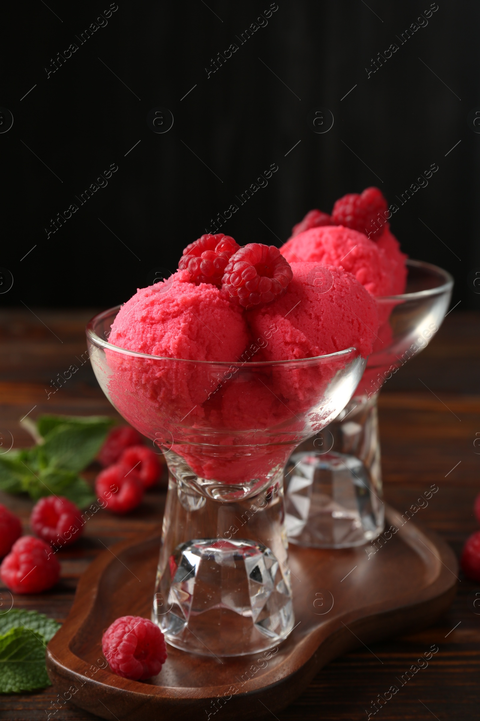 Delicious raspberry sorbet in dessert bowls, mint and fresh berries on wooden table against black background, closeup Photo of Delicious raspberry sorbet in dessert bowls, mint and fresh berries on wooden table against black background, closeup