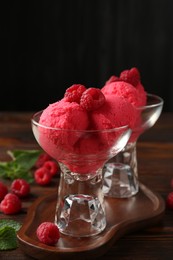 Photo of Delicious raspberry sorbet in dessert bowls, mint and fresh berries on wooden table against black background, closeup