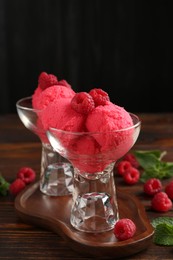 Photo of Delicious raspberry sorbet in dessert bowls, mint and fresh berries on wooden table against black background, closeup