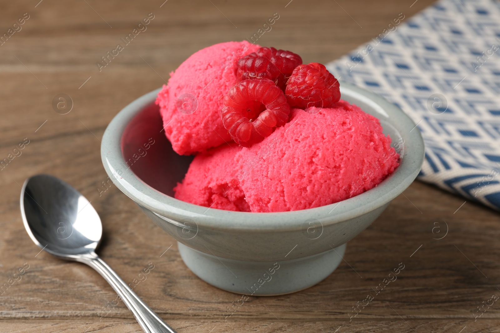 Photo of Delicious raspberry sorbet with fresh berries in bowl and spoon on wooden table, closeup