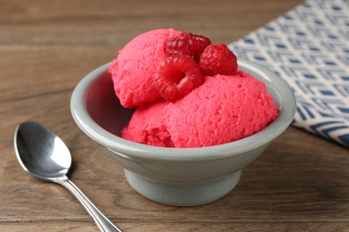 Photo of Delicious raspberry sorbet with fresh berries in bowl and spoon on wooden table, closeup