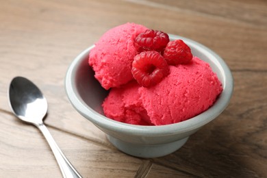 Photo of Delicious raspberry sorbet with fresh berries in bowl and spoon on wooden table, closeup