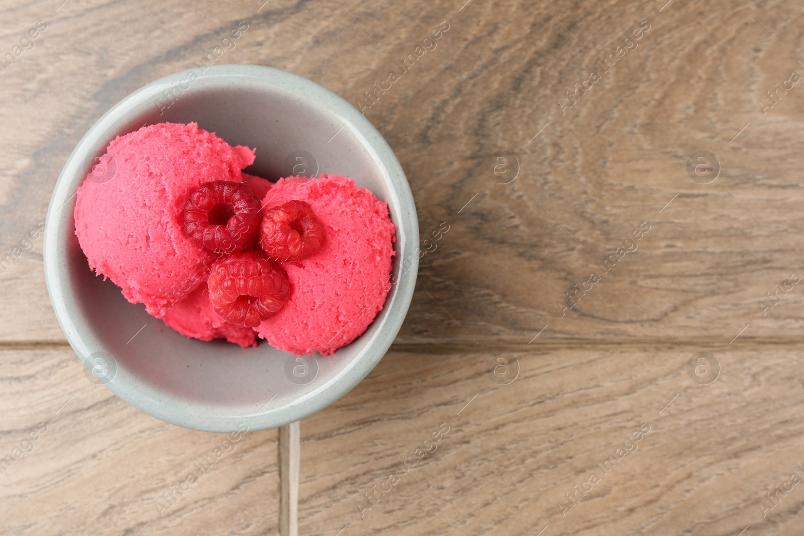 Photo of Delicious raspberry sorbet with fresh berries in bowl on wooden table, top view. Space for text